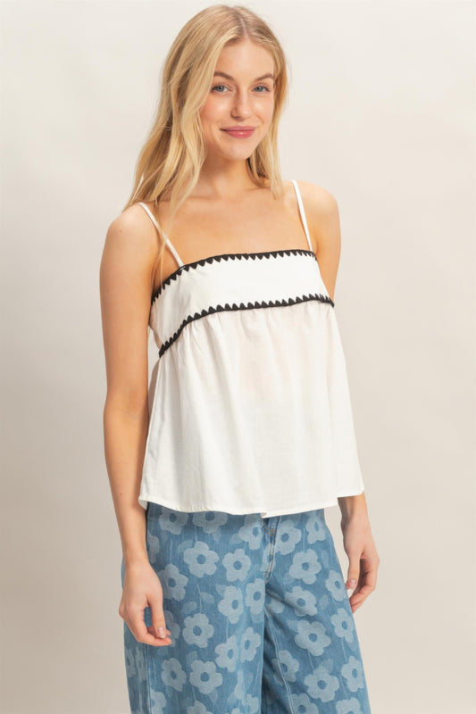 Haut babydoll blanc sans manches, bretelles fines et volants avec bordure noire.