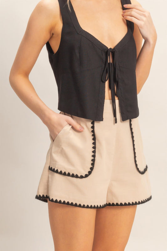 Short taille haute beige à bordure festonnée noire, poches plaquées contrastées.