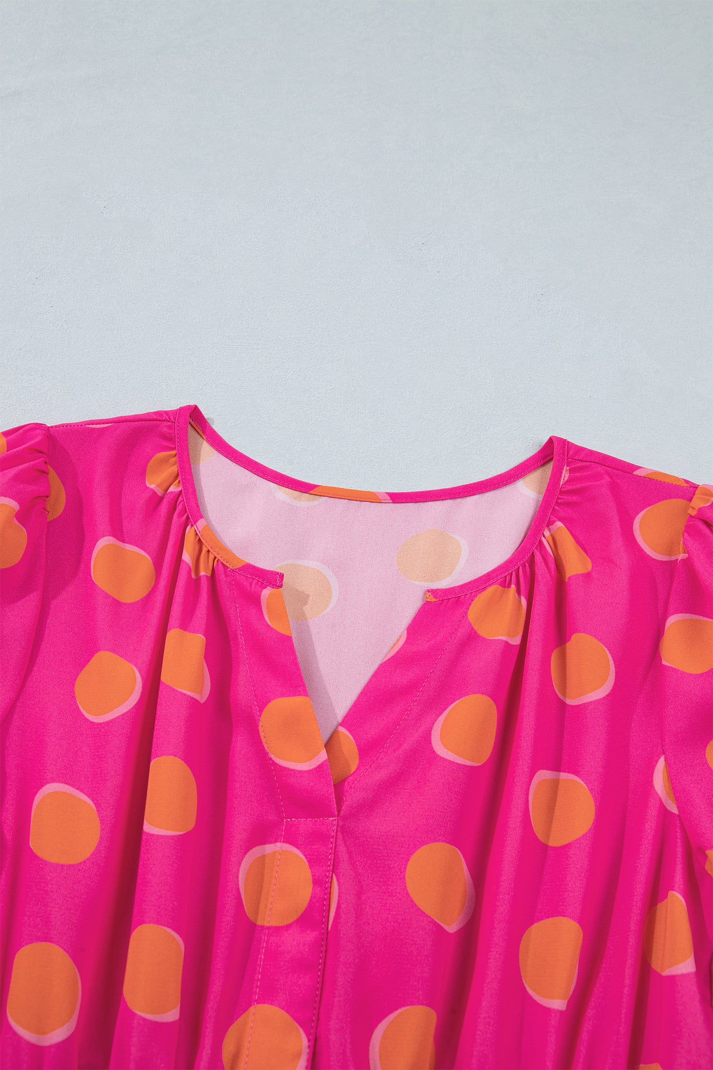 Encolure V de robe rose à pois jaune, tissu fluide et empiècement transparent.