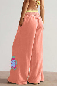 Pantalon ample corail avec fleurs sur les côtés, taille élastique, cordon et coupe large.