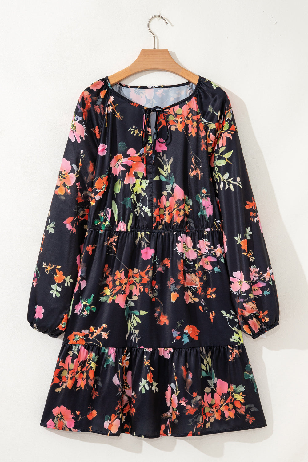 Robe noire fleurie sur cintre, col noué, manches longues et jupe à volants.