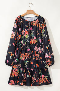 Robe noire fleurie sur cintre, col noué, manches longues et jupe à volants.