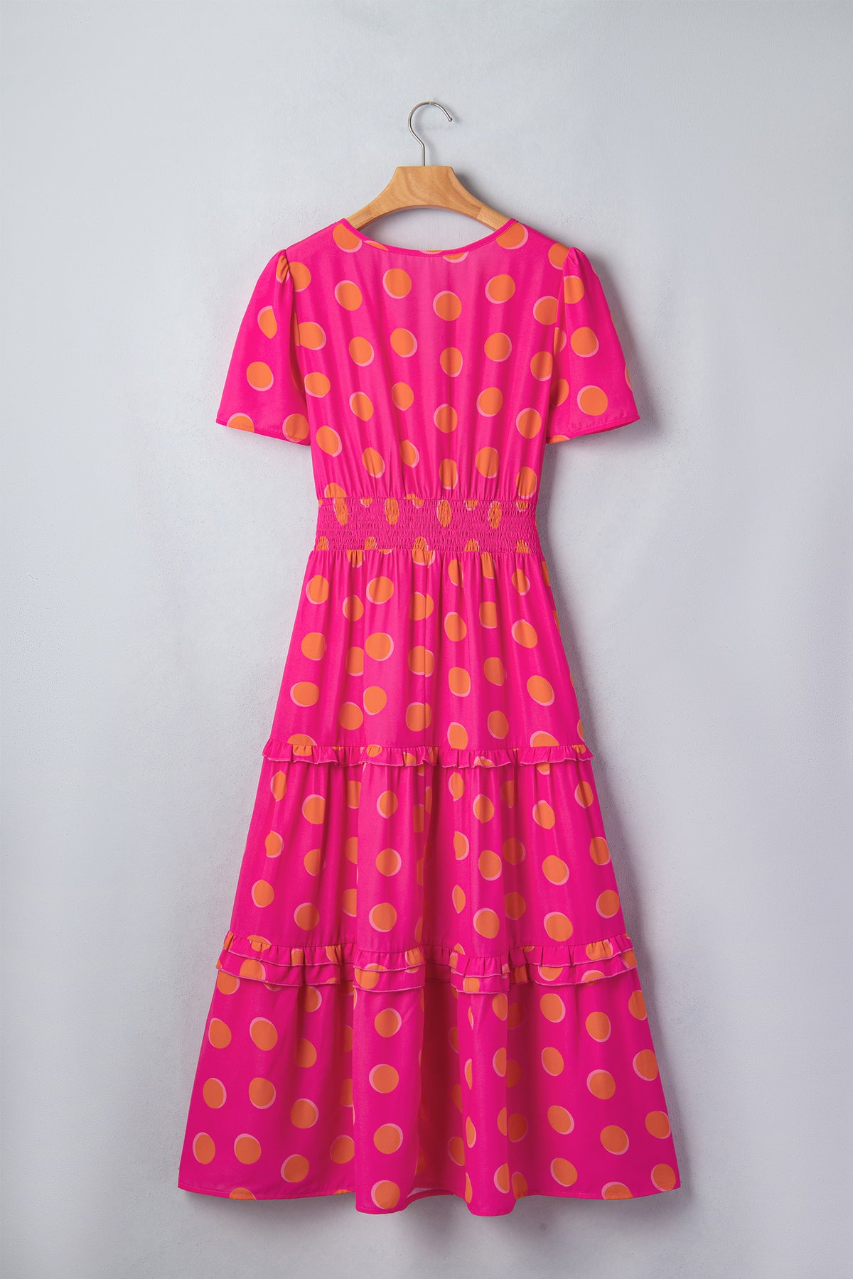 Robe rose à pois jaune sur cintre, encolure V au dos, volants étagés.