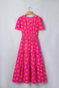 Robe rose à pois jaune sur cintre, encolure V au dos, volants étagés.