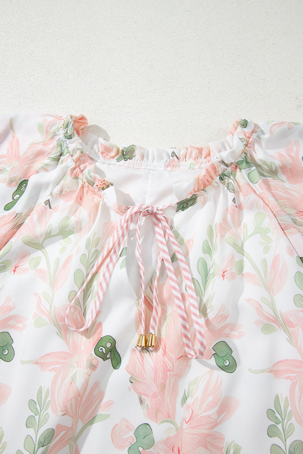 Robe courte rose à fleurs, encolure froncée avec nœud rayé au centre.
