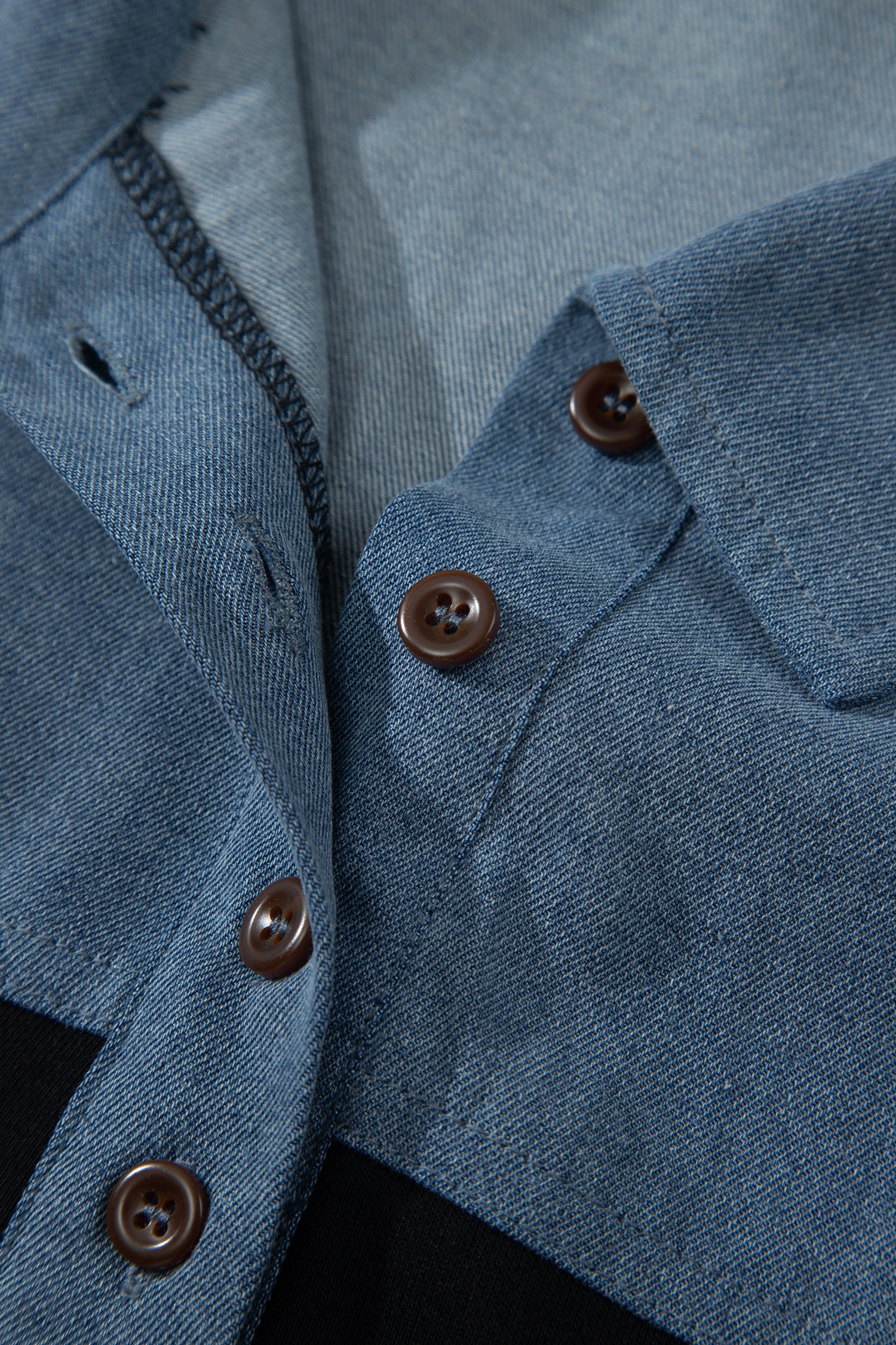 Haut polo bicolore en denim, gros plan patte boutonnée et col relevé.