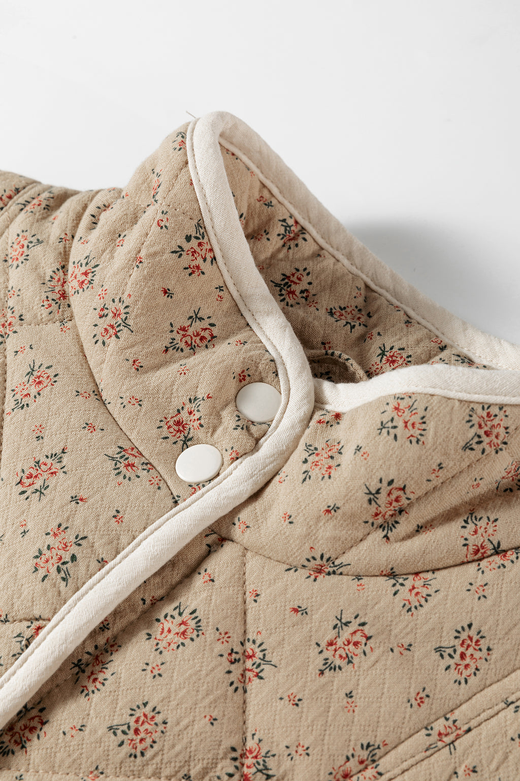 Veste matelassée beige à motif floral, col bordé de blanc et bouton pression visible