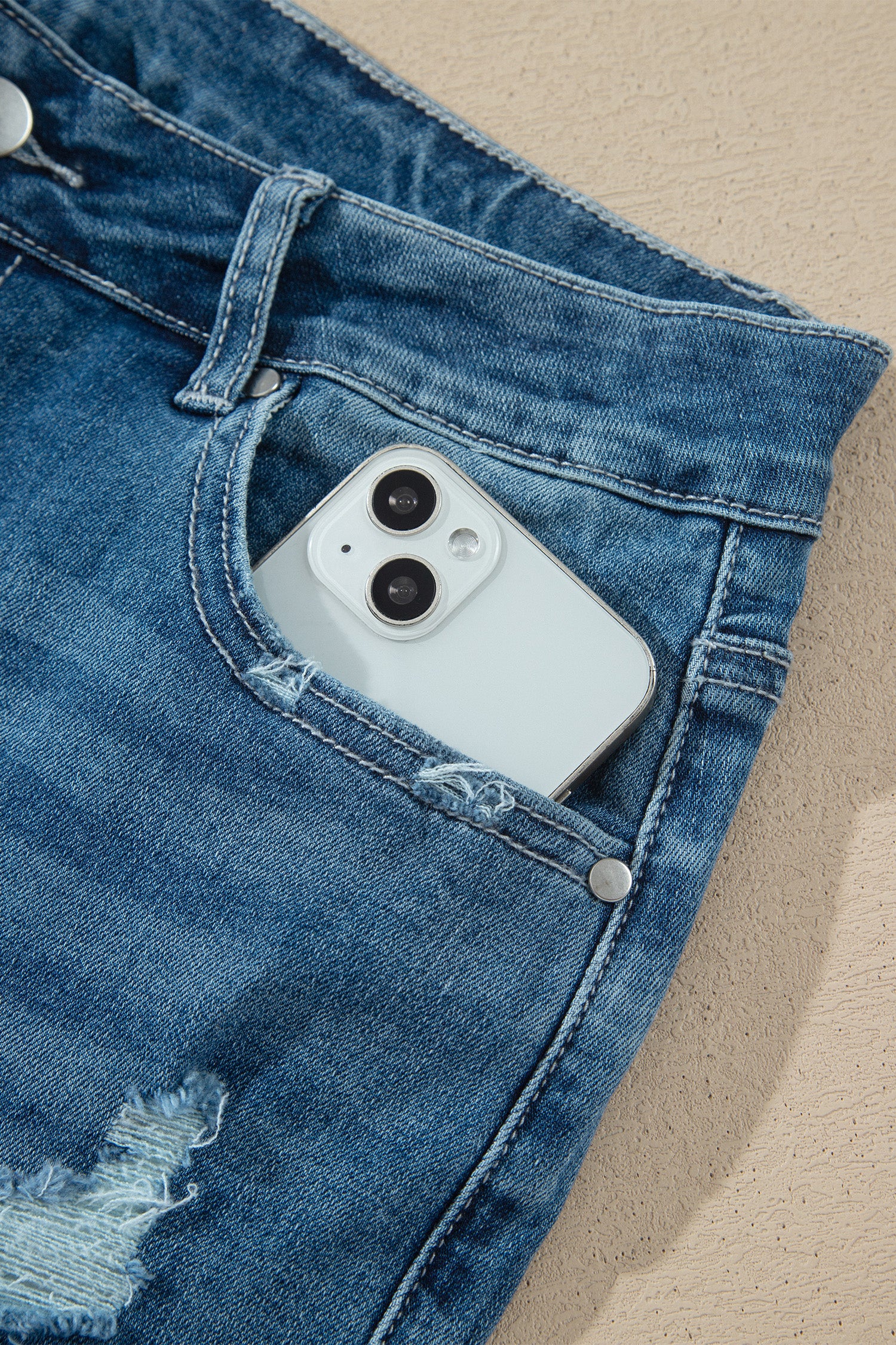 Détail poche jean taille haute bleu moyen, bouton, téléphone dans la poche.
