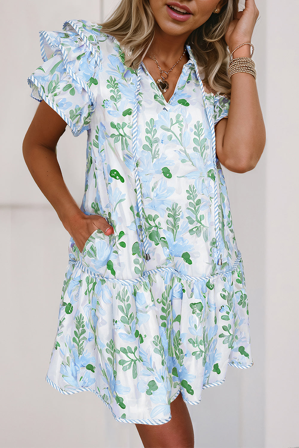 Robe courte blanche à motifs végétaux bleu clair et verts, col V, manches volantées.