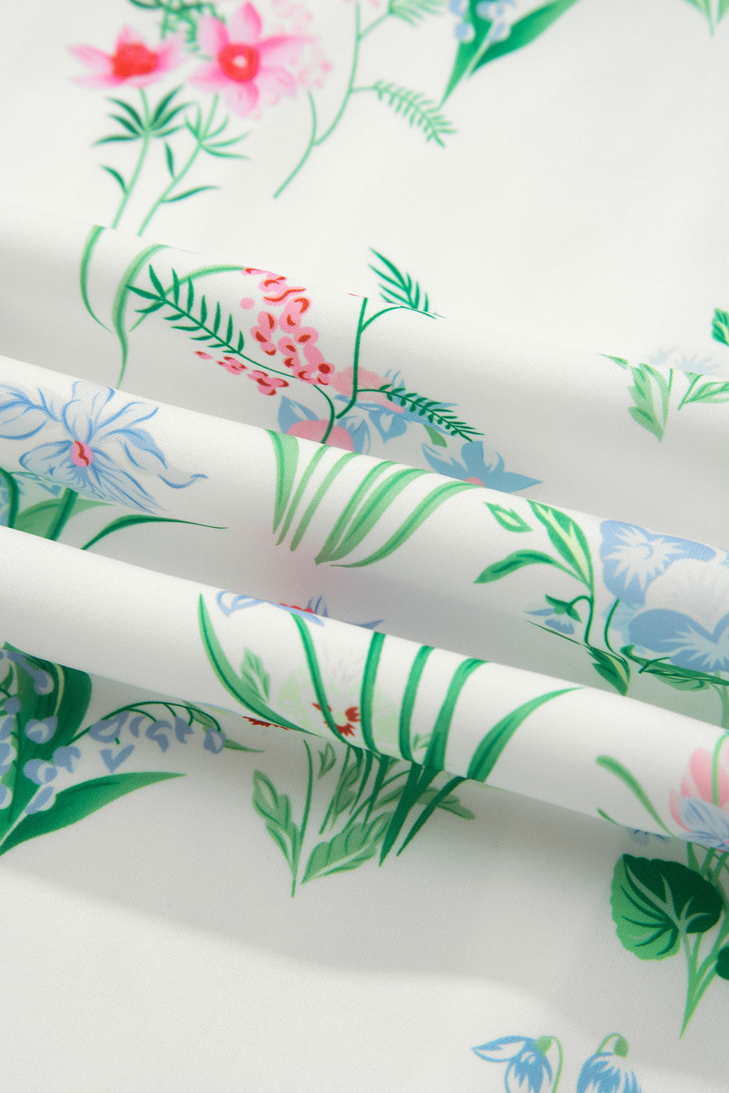 Détail tissu de robe : imprimé floral et feuillages verts, fond clair