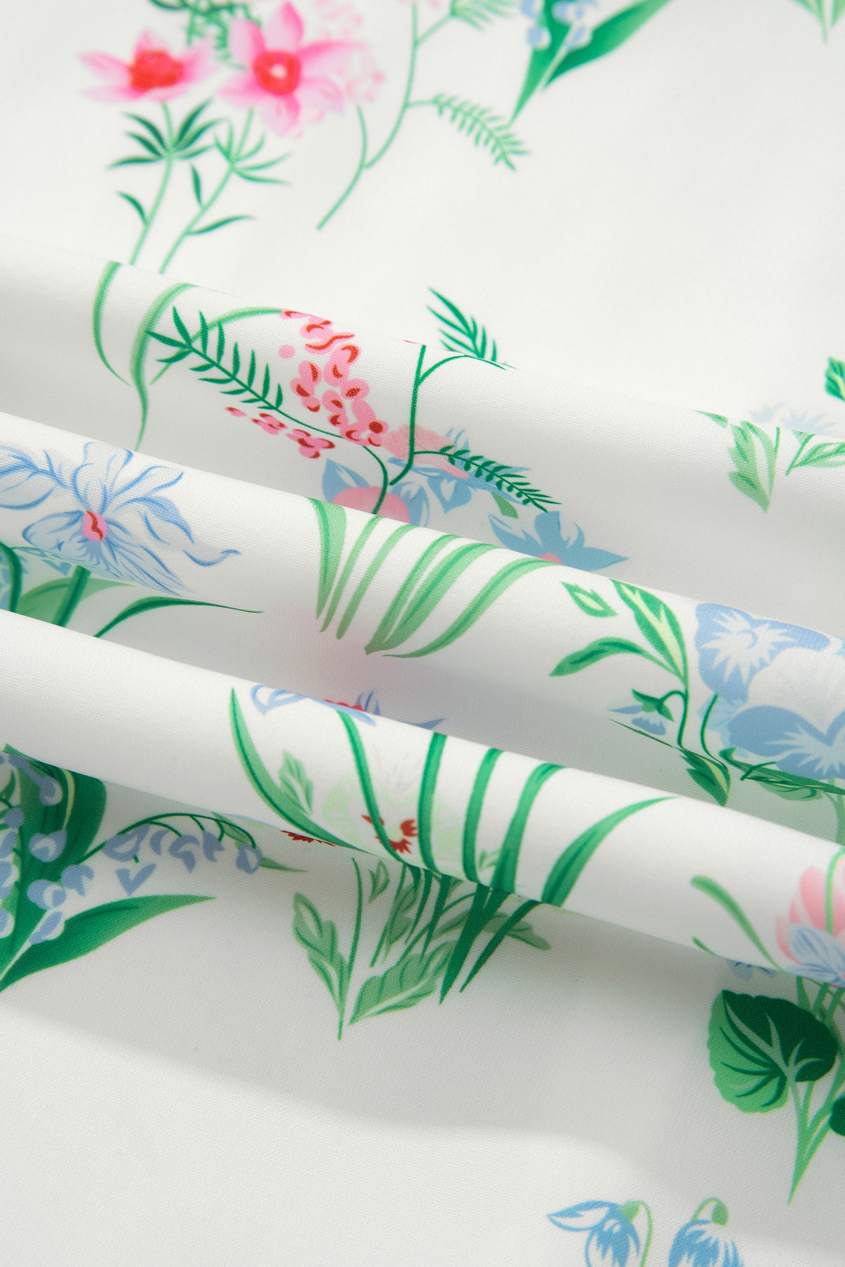 Détail tissu de robe : imprimé floral et feuillages verts, fond clair
