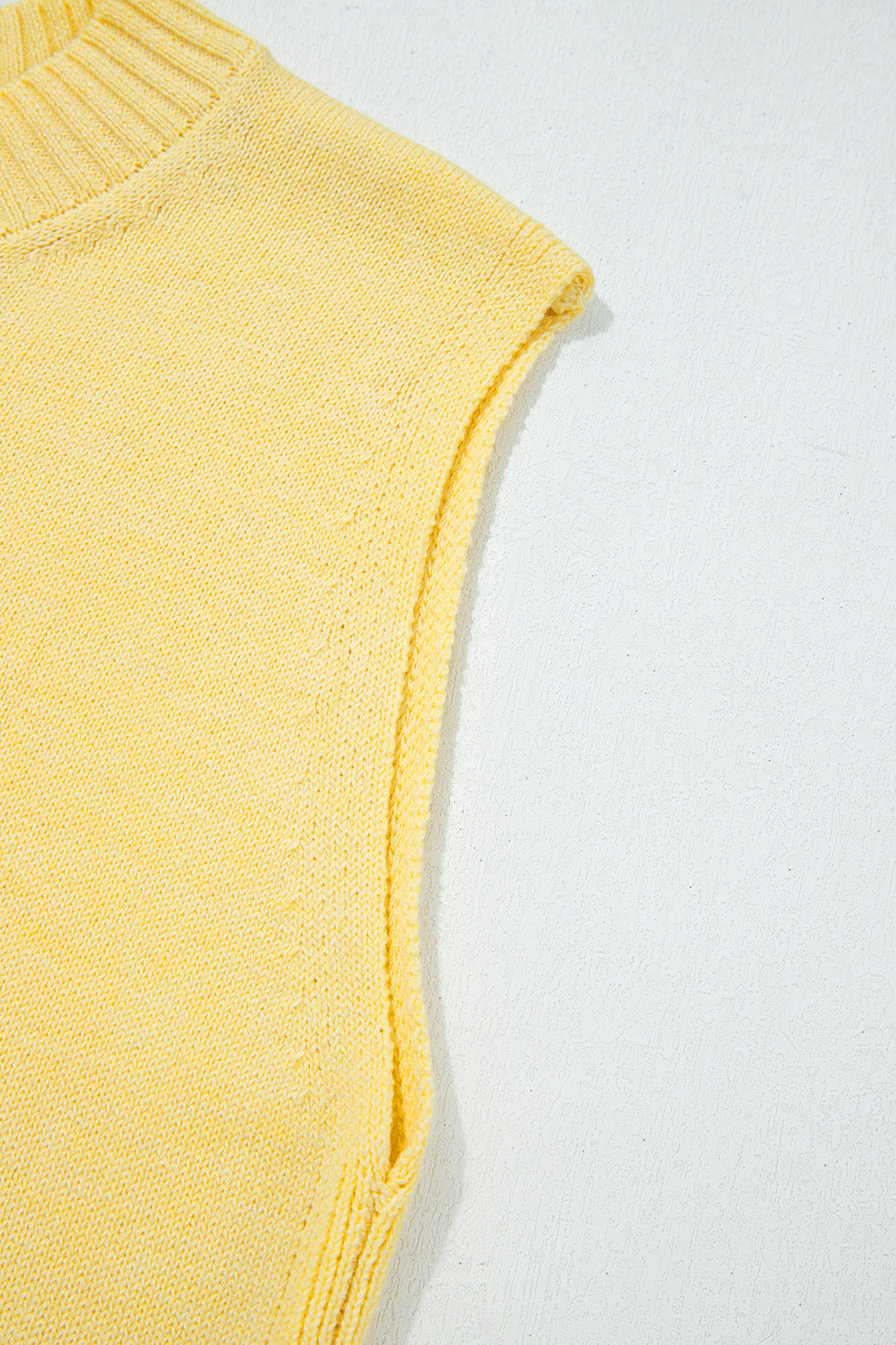 Détail de l’ourlet du haut sans manches en maille jaune, bord côtelé.