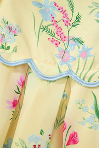 Détail ourlet festonné bleu clair sur robe crème à fleurs colorées, base évasée.