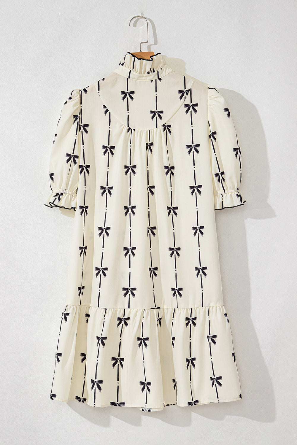 Robe courte sur cintre, dos crème à motifs nœuds papillon, bas à volants.