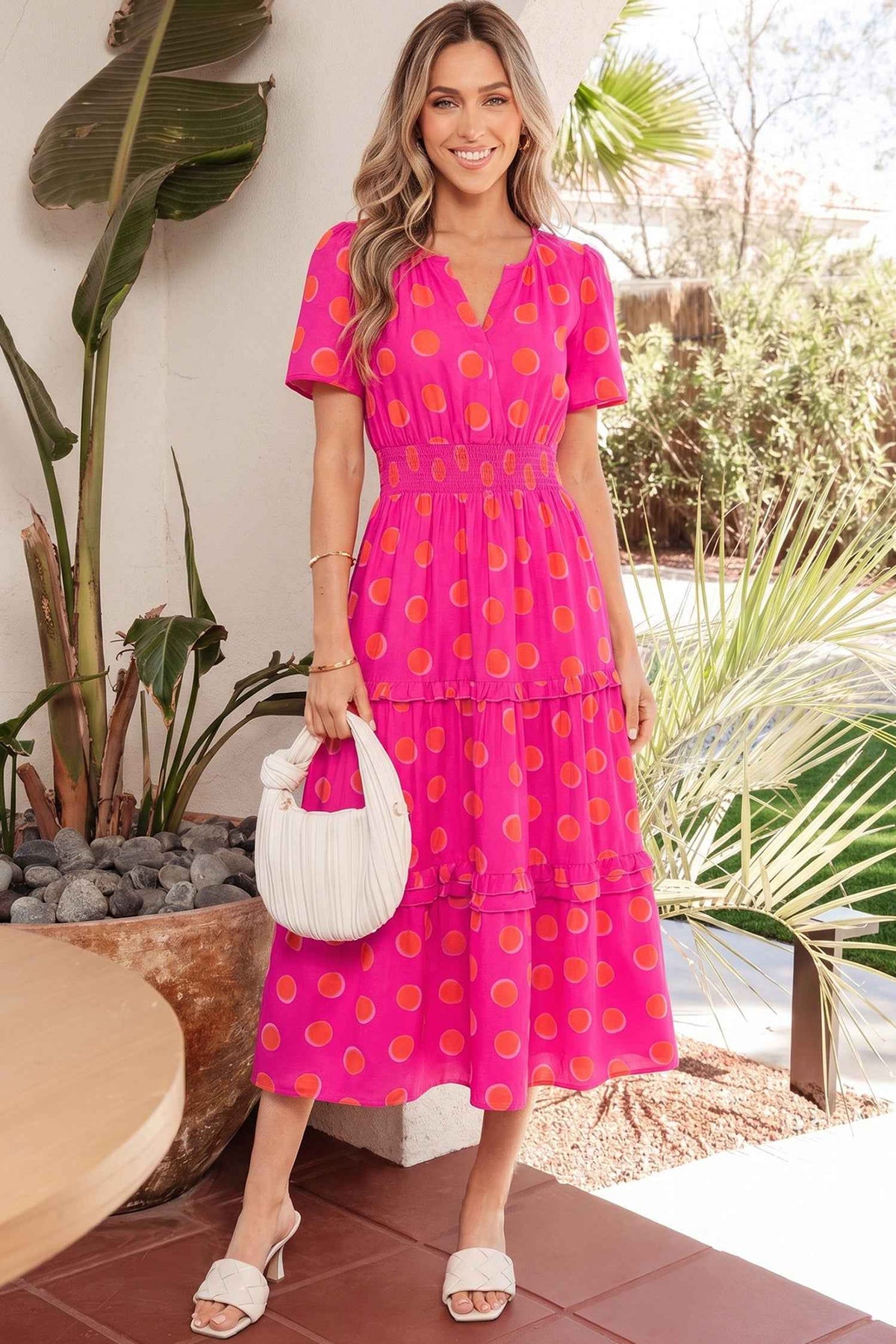 Robe mi-longue rose à pois jaune, encolure V et volants étagés.
