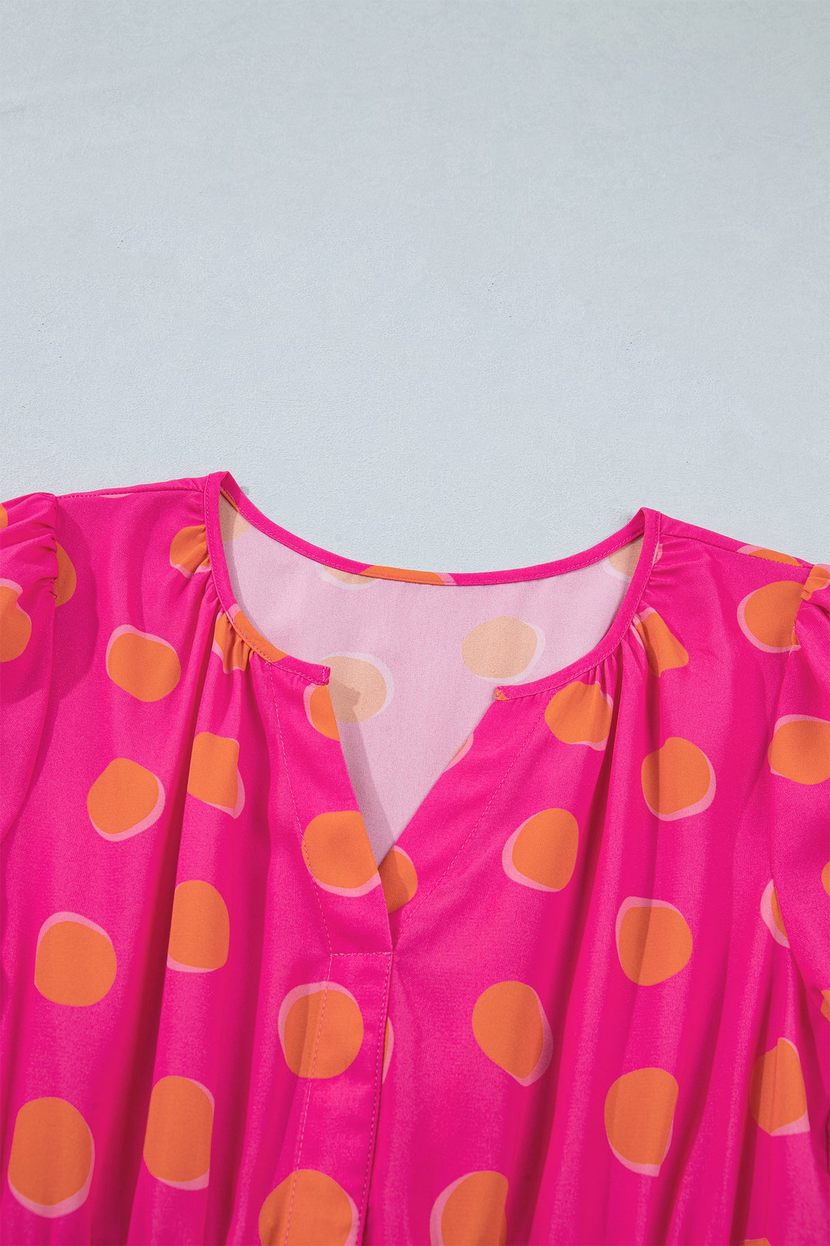 Encolure V de robe rose à pois jaune, tissu fluide et empiècement transparent.