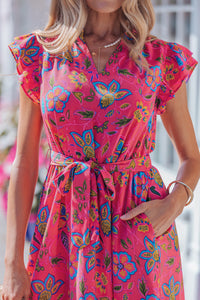 Robe fuchsia fleurie, décolleté en V, ceinture à nouer, manches volantées, motif coloré.