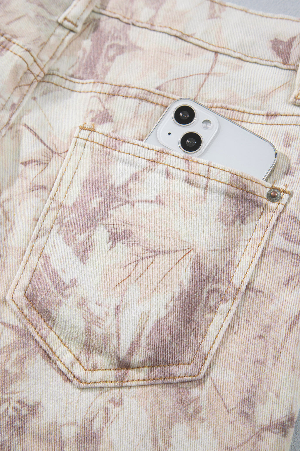 Jean large femme motif camouflage rose clair, poche avant et surpiqûres visibles.