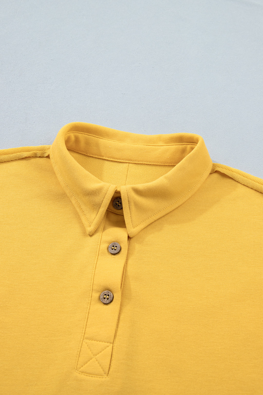 Polo jaune de l’ensemble pour femme : col avec patte boutonnée, empiècement en triangle.