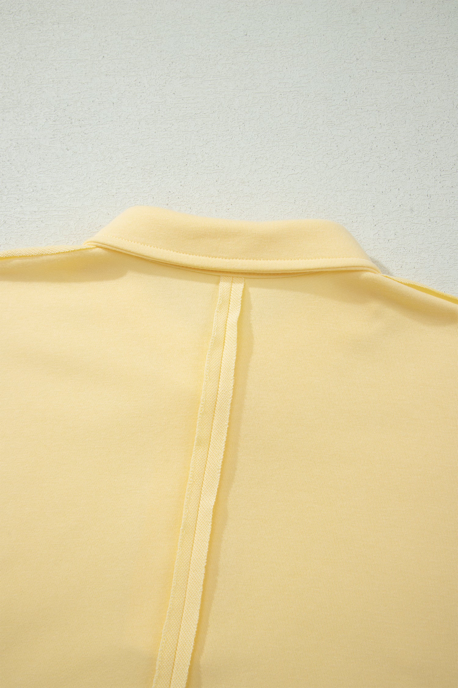 Dos du polo jaune crème avec ouverture/fente centrale et ourlet