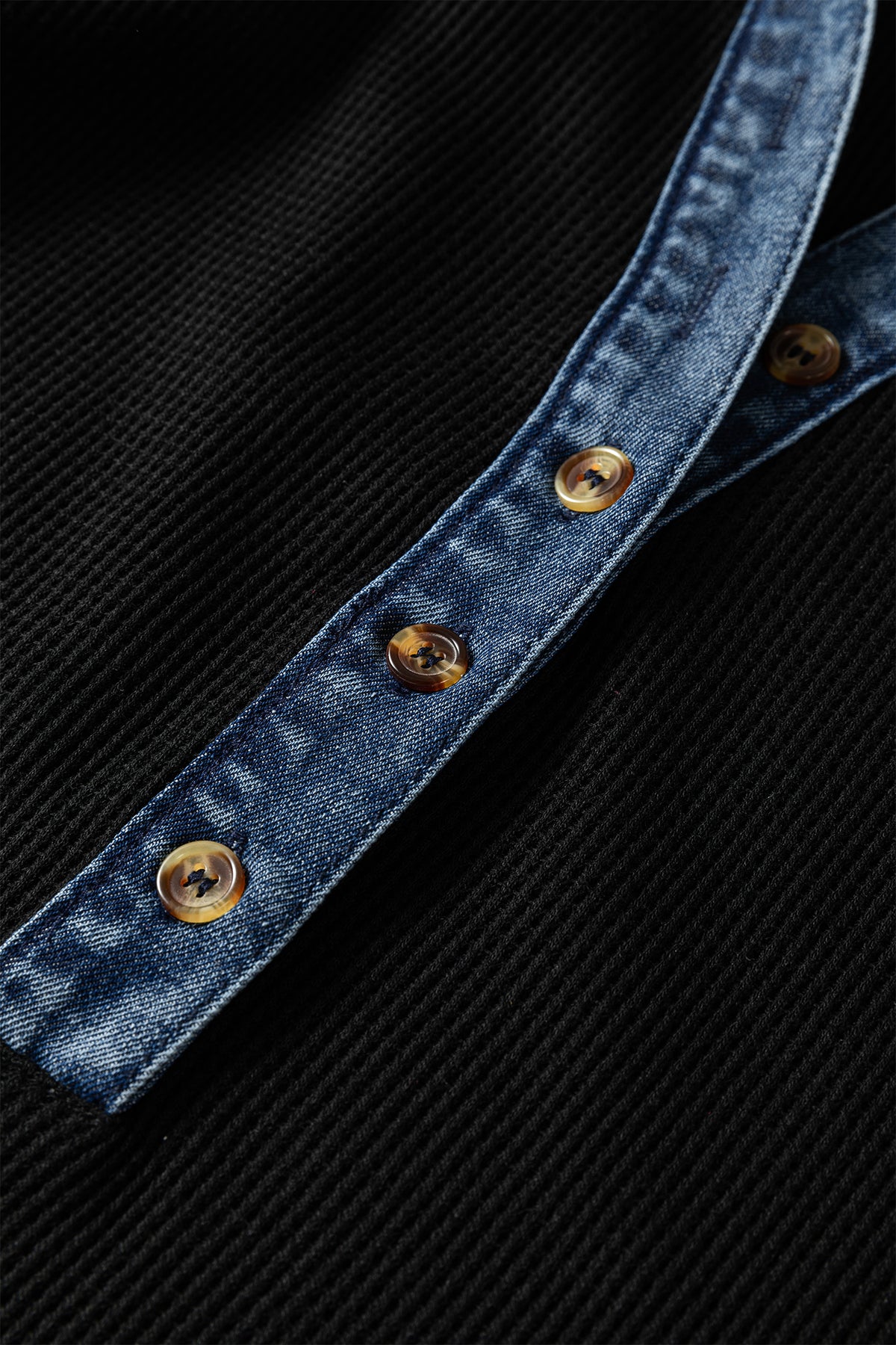 Bande en denim bleu boutonnée avec boutons dorés sur robe noire.