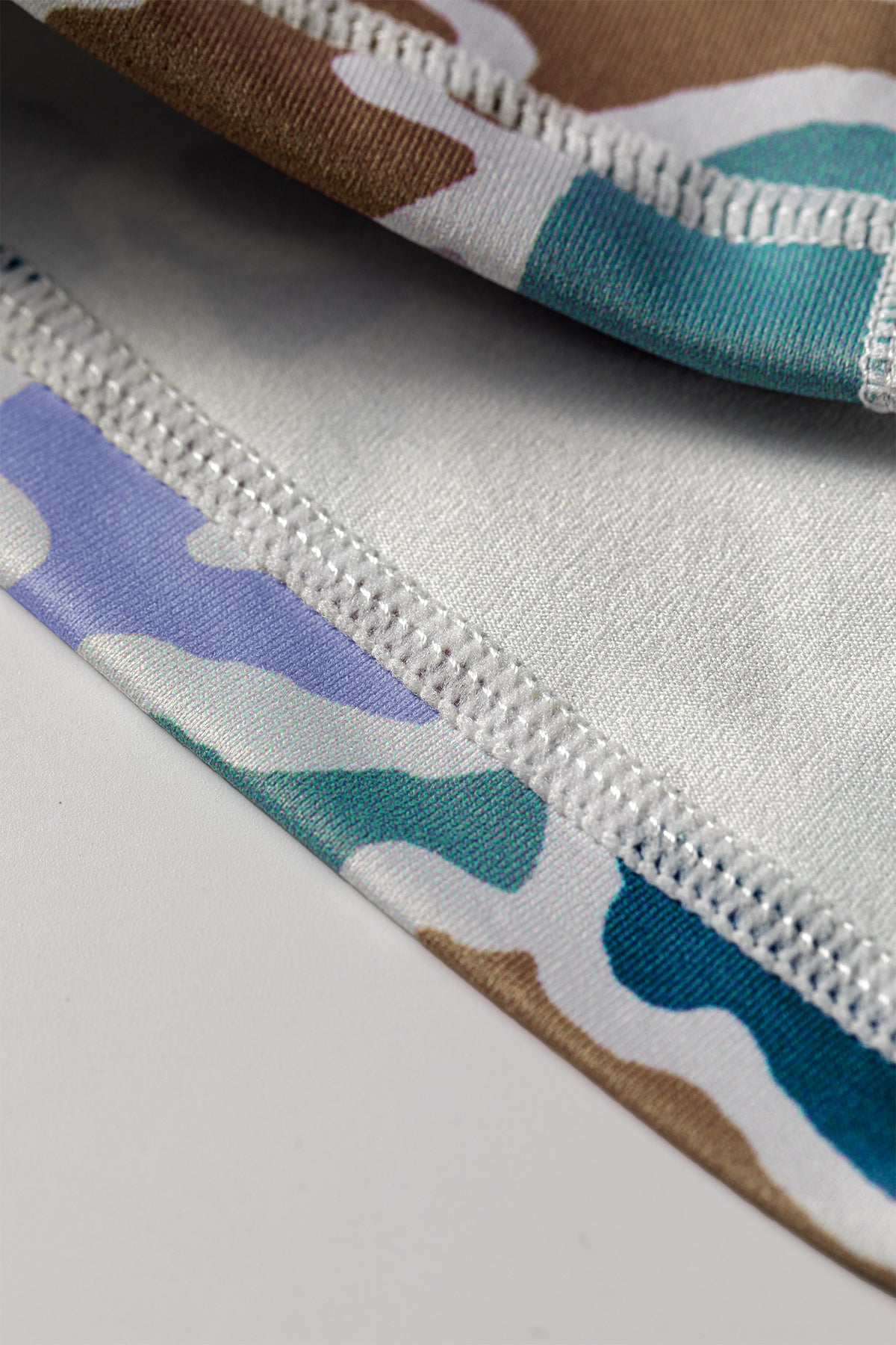 Couture d’ourlet et élastique blanc sur short cycliste imprimé camouflage multicolore.