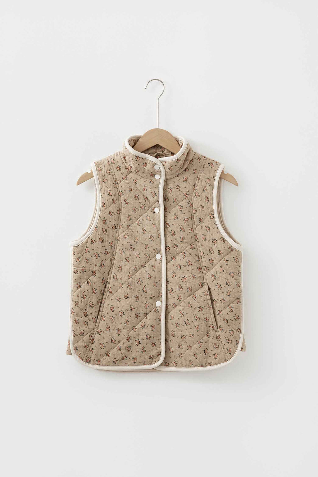 Veste matelassée beige à motif floral sur cintre, col montant, boutons pression, sans manches