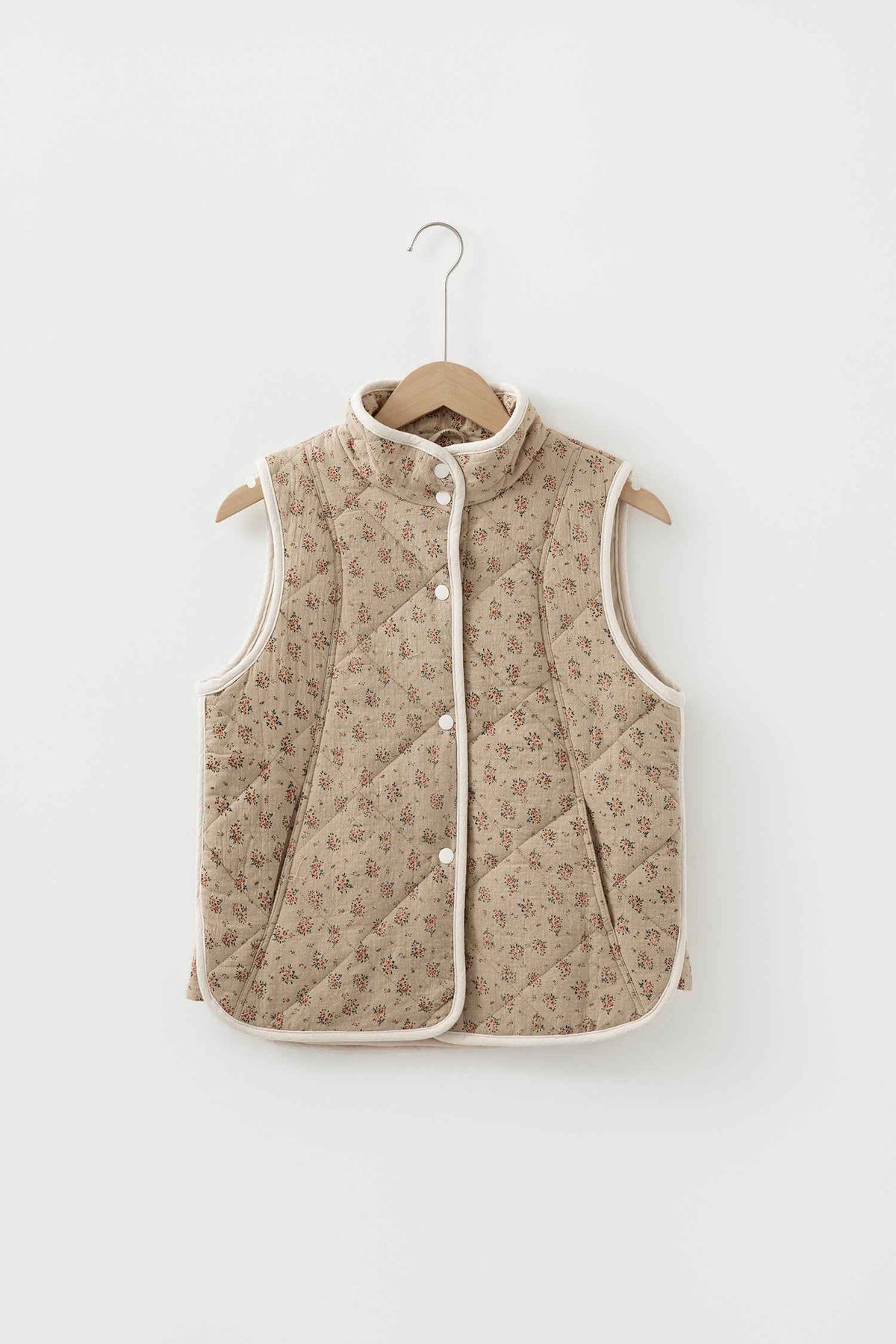 Veste matelassée beige à motif floral sur cintre, col montant, boutons pression, sans manches