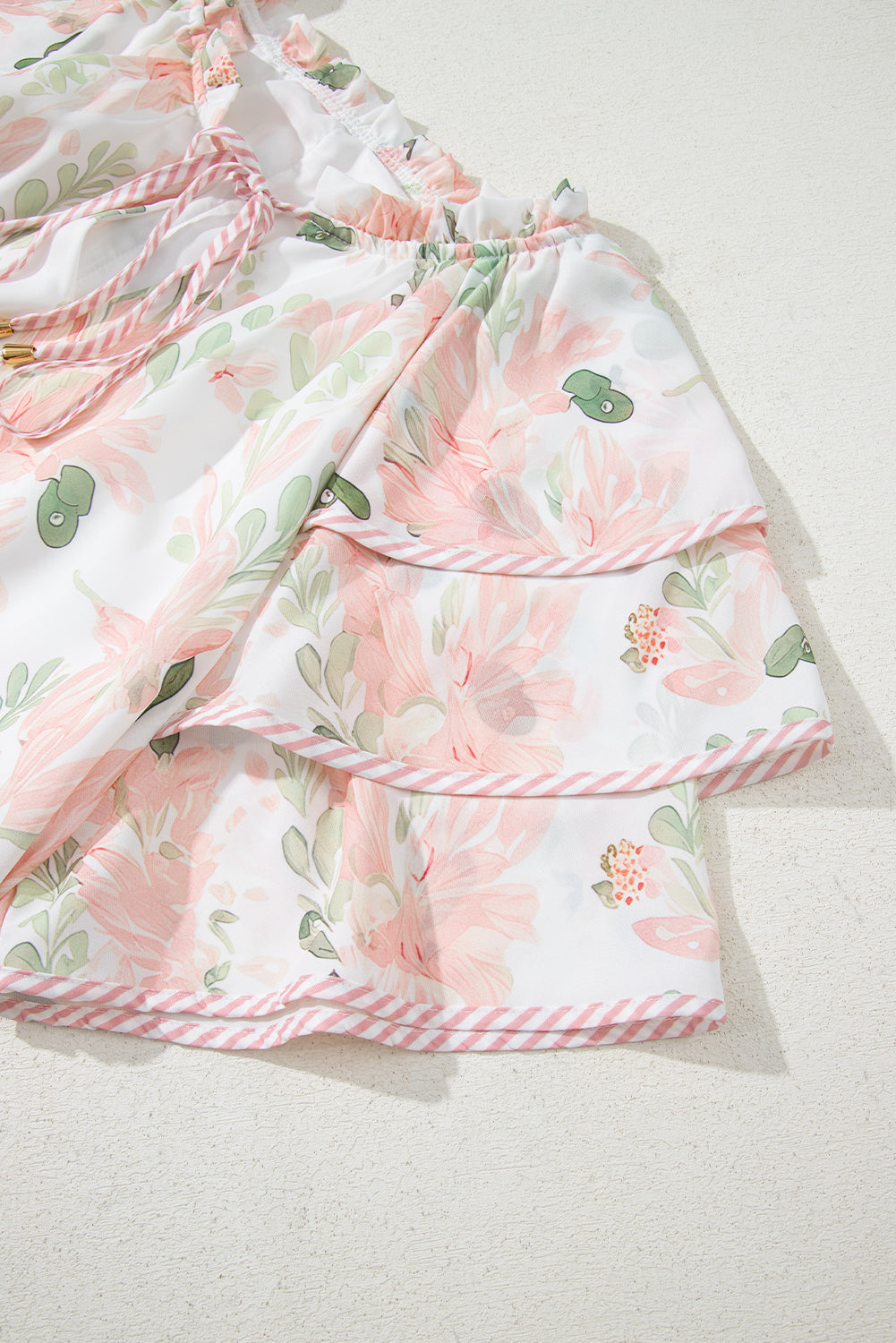 Robe courte rose à fleurs, jupe à volants superposés et nœud à l’encolure.