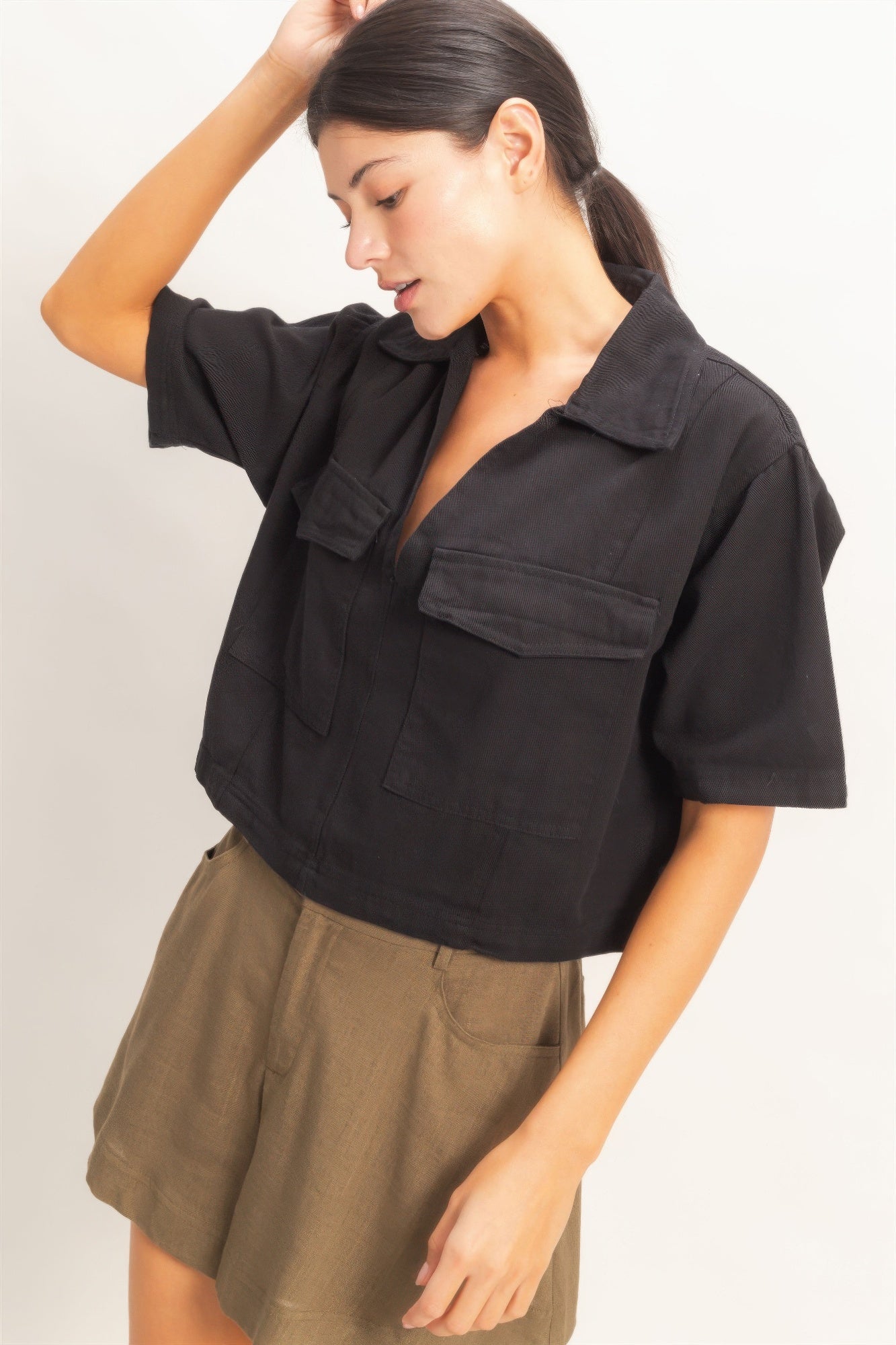 Haut femme en coton noir, col V, manches courtes, poches plaquées, empiècements.