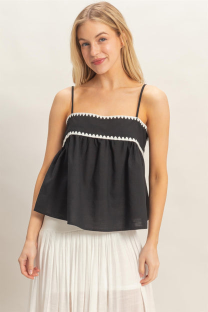 Débardeur babydoll noir sans manches, bretelles fines, volants et bordure zigzag blanche.