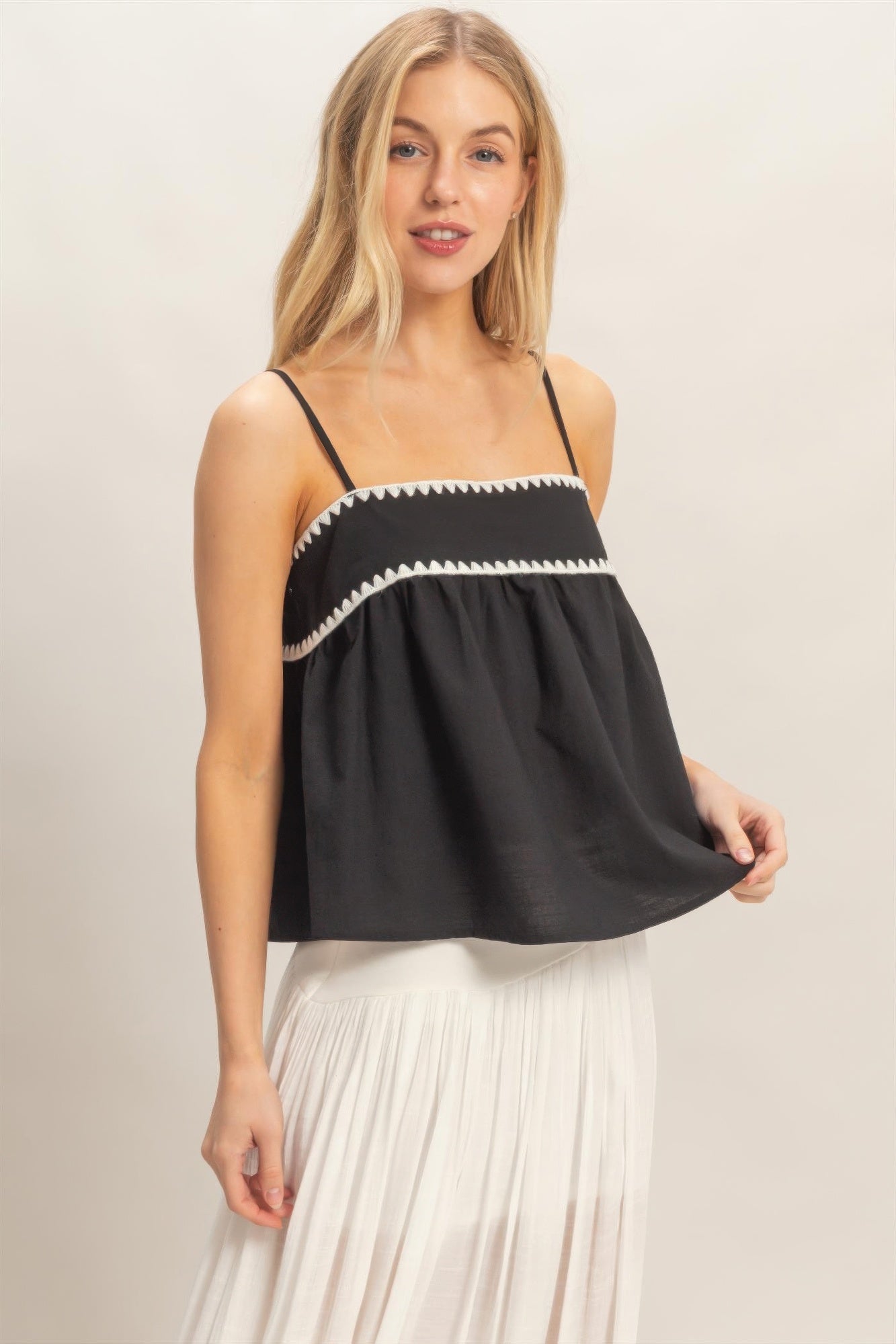 Débardeur babydoll noir sans manches, bordure zigzag blanc, silhouette évasée.
