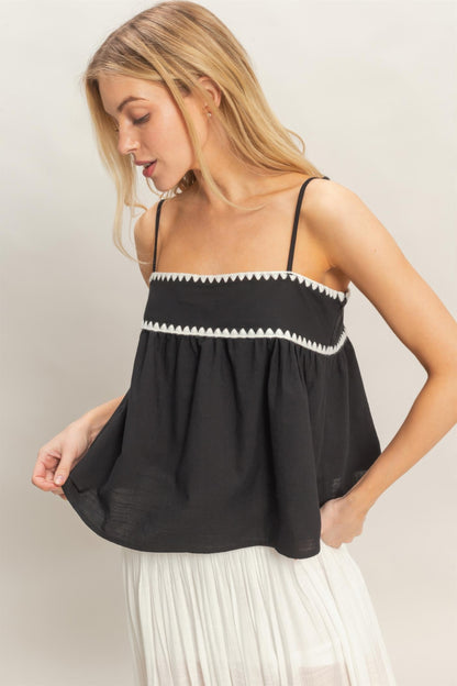 Débardeur babydoll noir sans manches, bordure zigzag blanche, volant froncé sous la poitrine.
