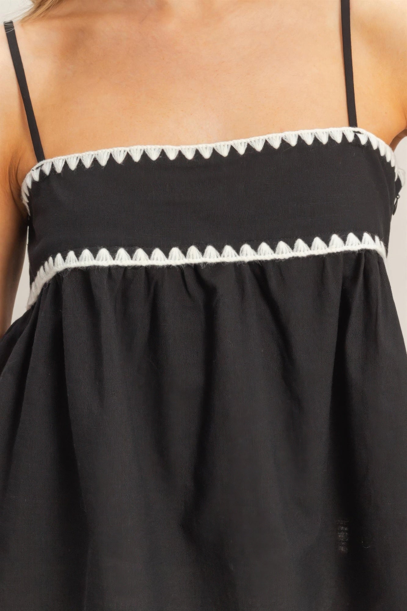 Débardeur babydoll noir, bordures zigzag blanc, haut froncé avec bretelles fines.