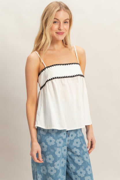 Haut babydoll blanc sans manches, bretelles fines et volants avec bordure noire.