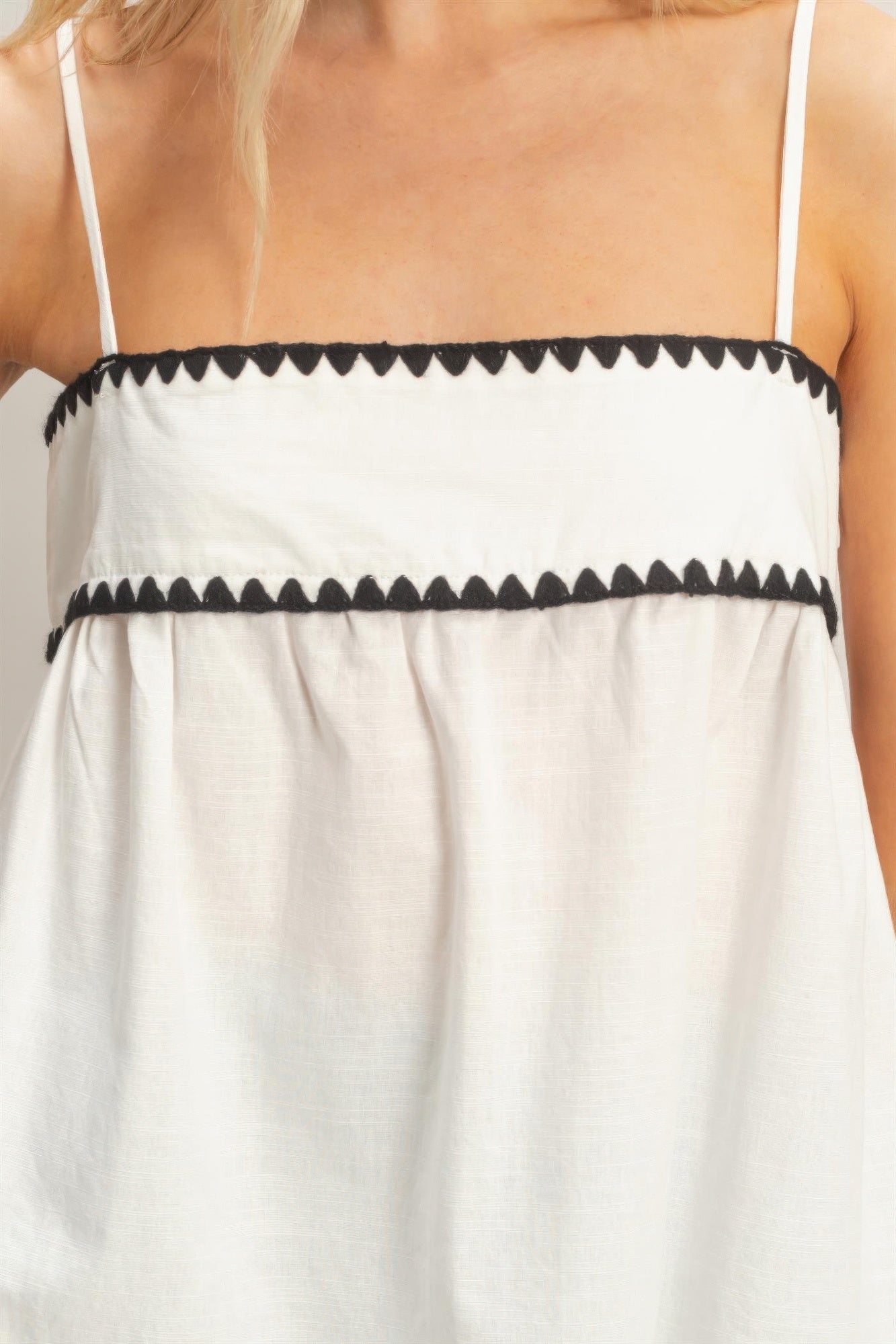 Haut babydoll blanc sans manches, bretelles fines et bordure noire décorative.