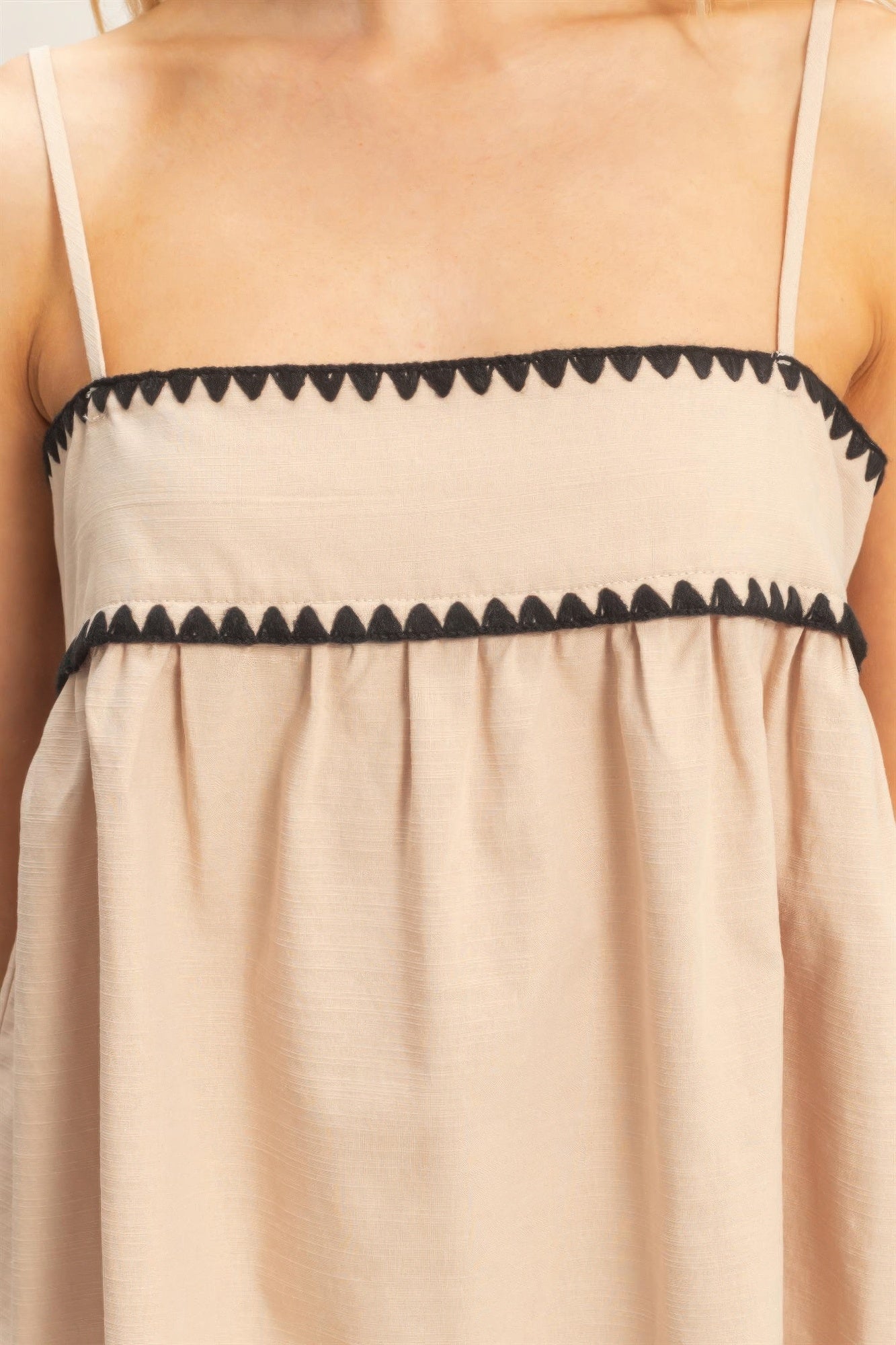 Débardeur babydoll beige sans manches, fines bretelles, bordure contrastée zigzag.