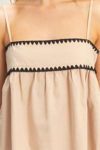 Débardeur babydoll beige sans manches, fines bretelles, bordure contrastée zigzag.
