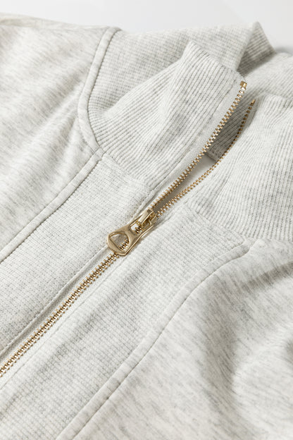 Détail ensemble : fermeture zippée dorée sur polo en tissu gris clair