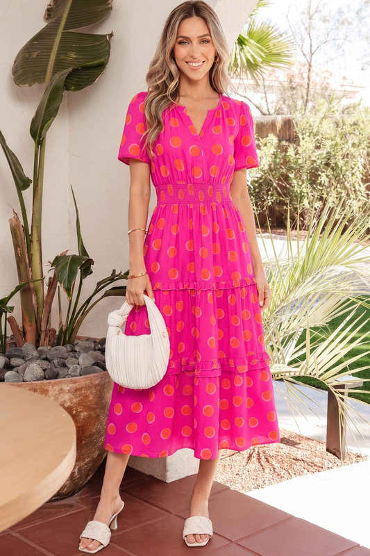 Robe mi-longue rose à pois jaune, encolure V et volants étagés.