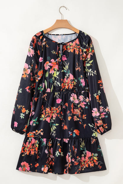 Robe noire fleurie sur cintre, col noué, manches longues et jupe à volants.