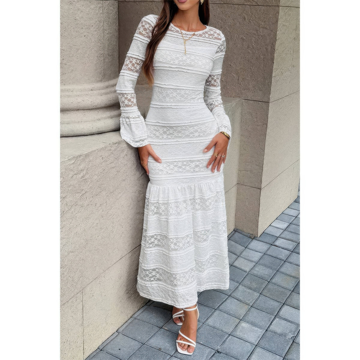Robe longue en dentelle blanche à encolure ronde, manches longues et ourlet volanté.