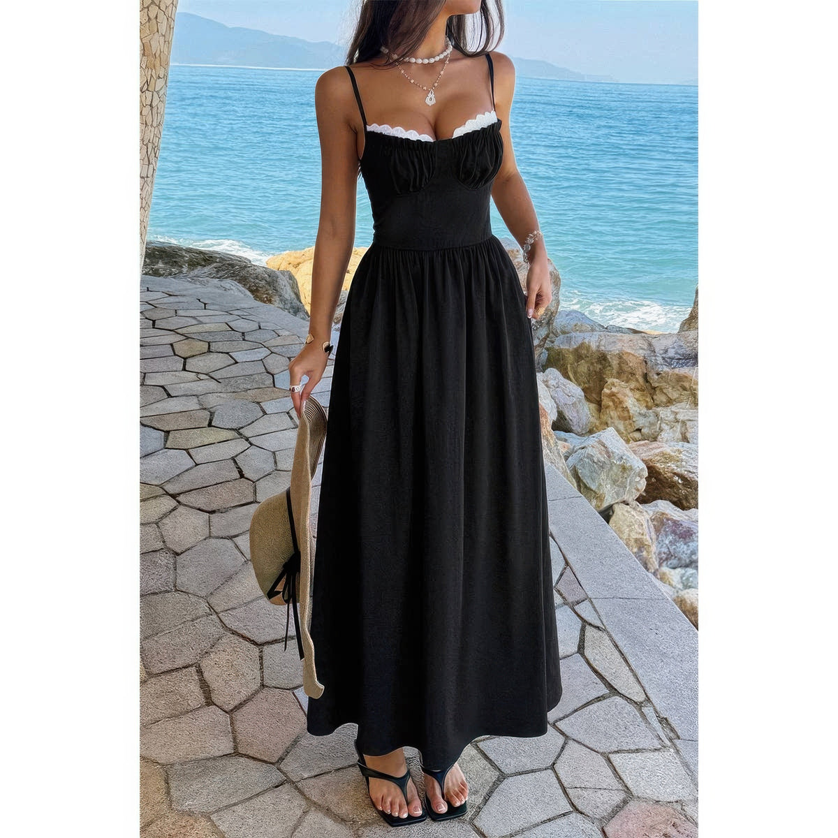 Robe longue noire à bretelles spaghetti, jupe ample froncée, bord dentelle blanche.