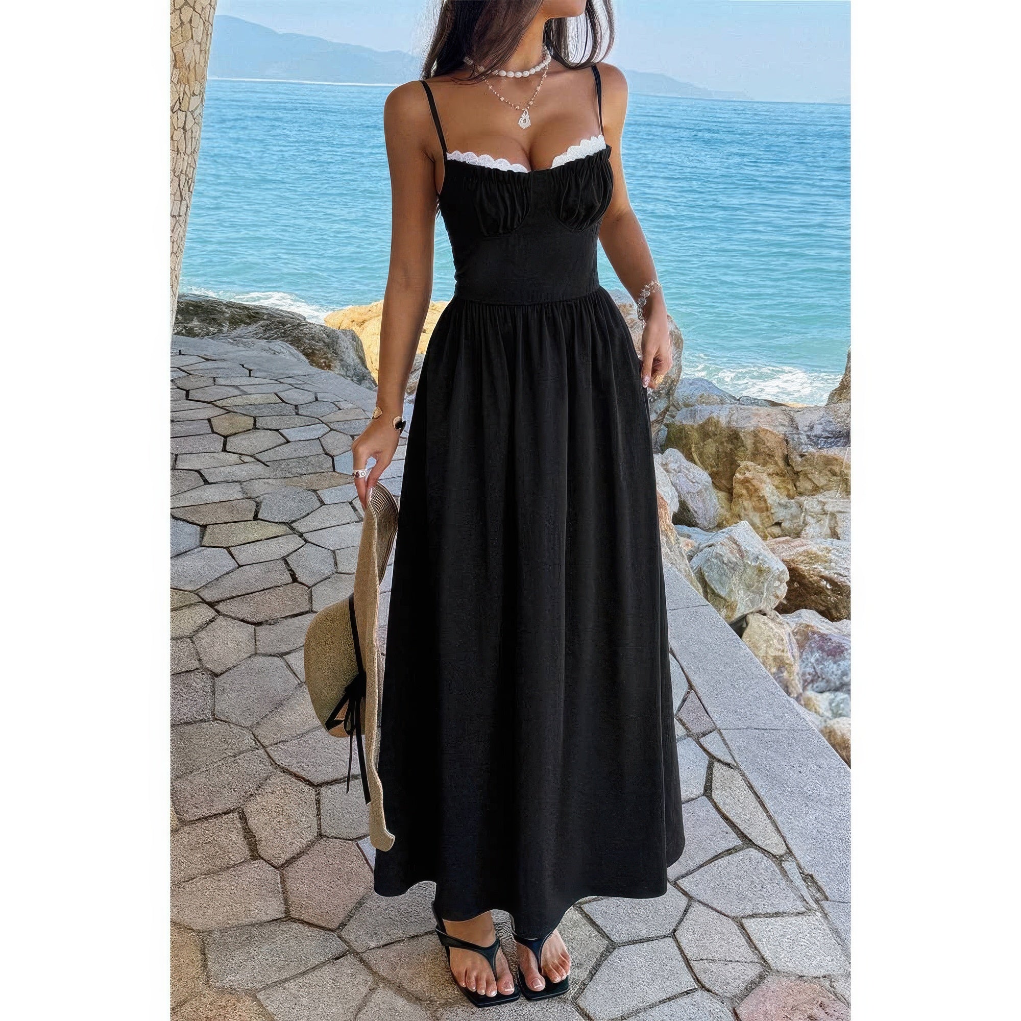Robe longue noire à bretelles spaghetti, jupe ample froncée, bord dentelle blanche.