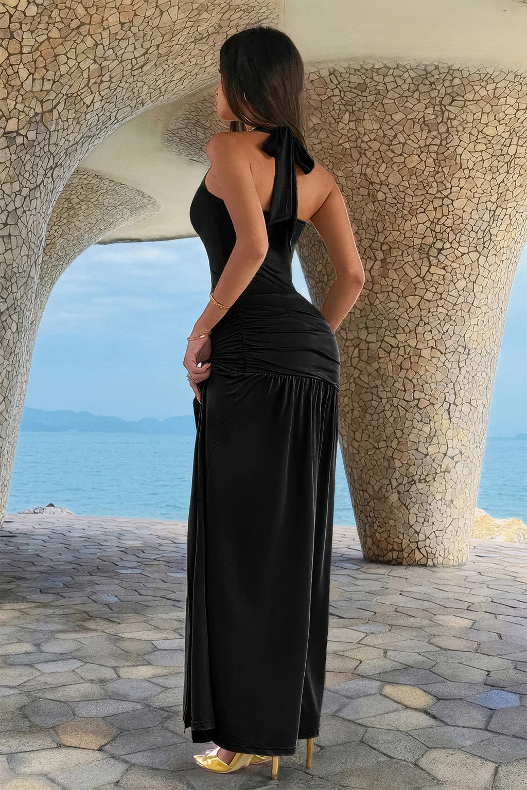 Robe maxi noire vue de dos, col halter, fente haute, fronces, ornement doré