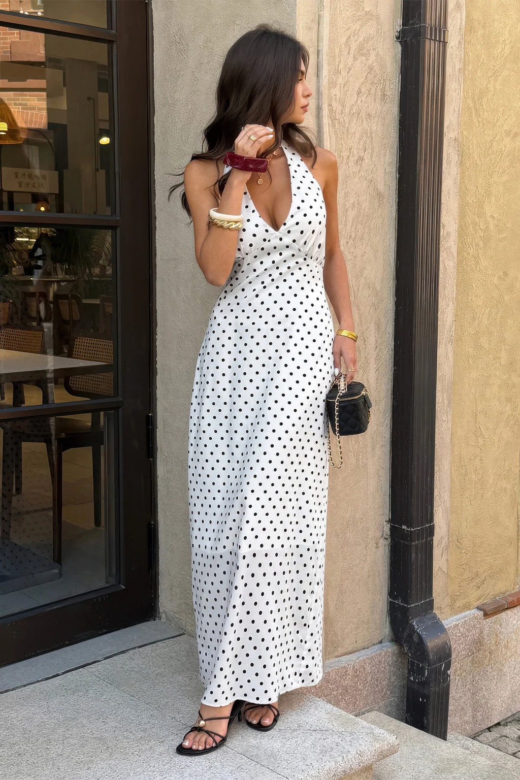 Robe longue sans manches blanche à pois noirs, encolure plongeante, coupe près du corps.