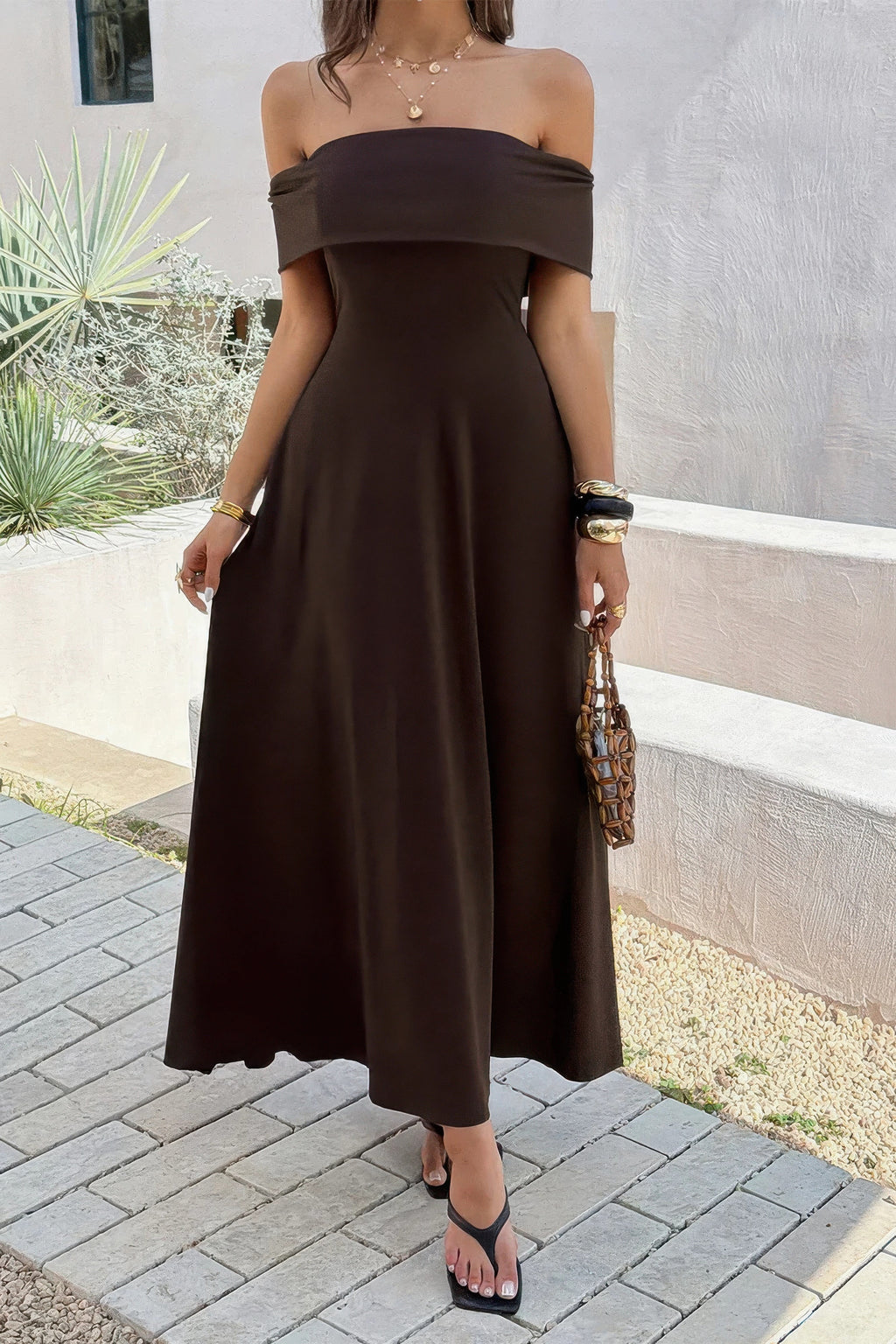 Robe maxi unie marron à épaules dénudées, coupe évasée et sans manches apparentes.