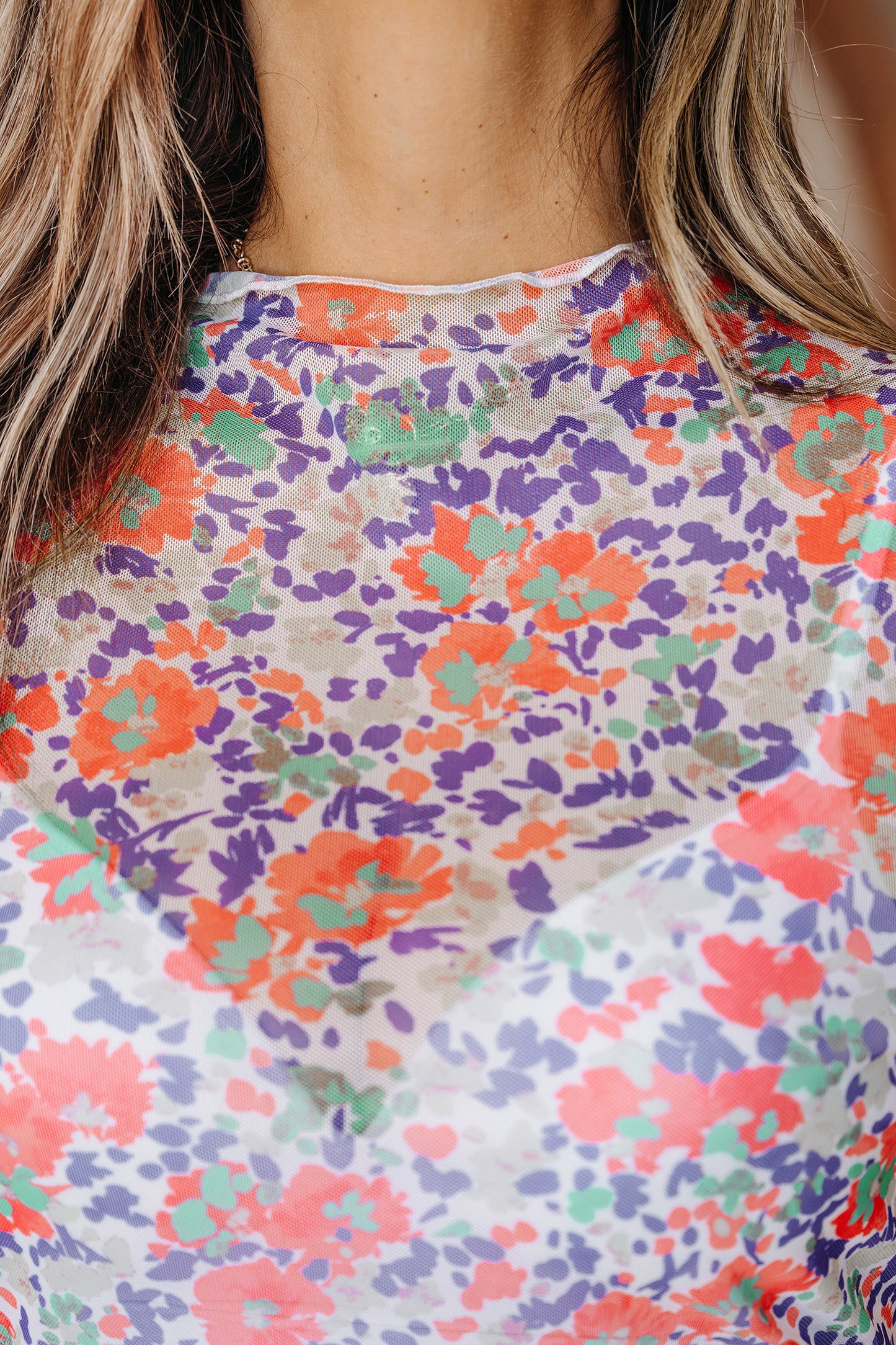 Détail du haut femme : col montant et maille à fleurs multicolores sur fond clair.