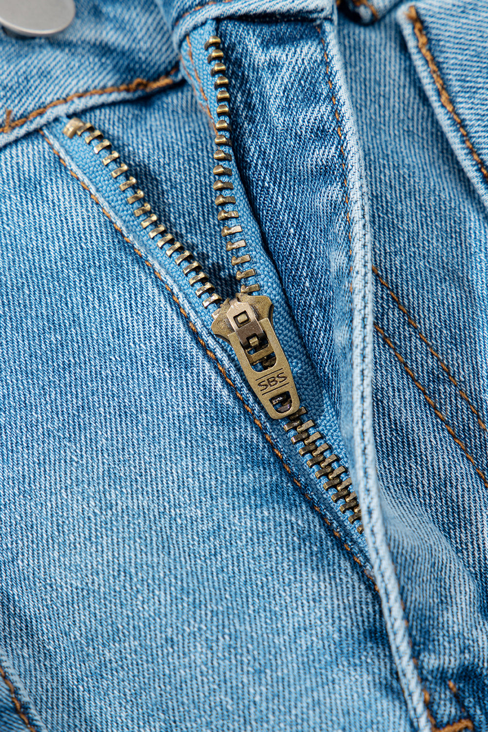 Fermeture éclair et surpiqûres sur jupe en jean bleu clair, détail de la tirette