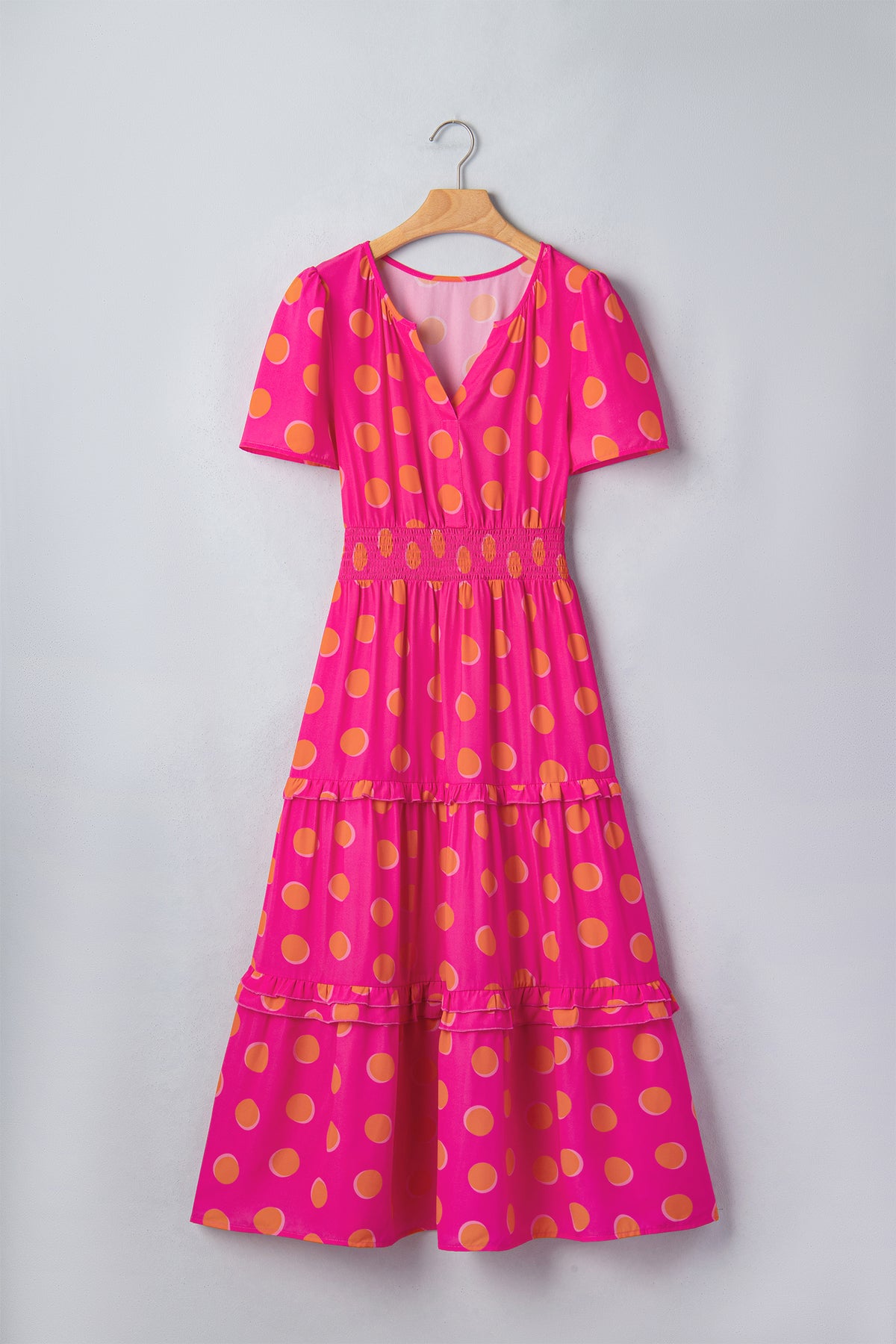 Robe rose à pois jaune sur cintre, encolure V, manches courtes, volants étagés.